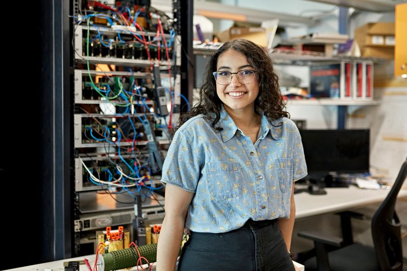Waist-up view of casually dressed woman standing in electrical engineering lab and smiling at camera. Property release attached.