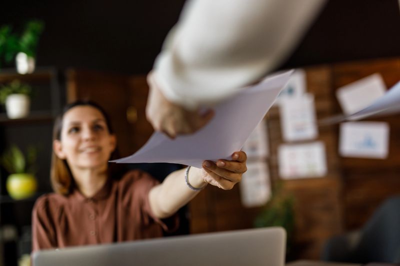 Low angle view of unrecognizable businesswoman handing a document to her coworker when co-working in a modern office space.