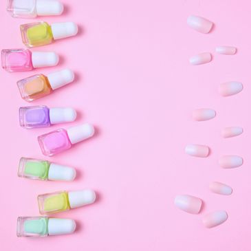 Colorful nail polish bottles and false nails on a pink background.