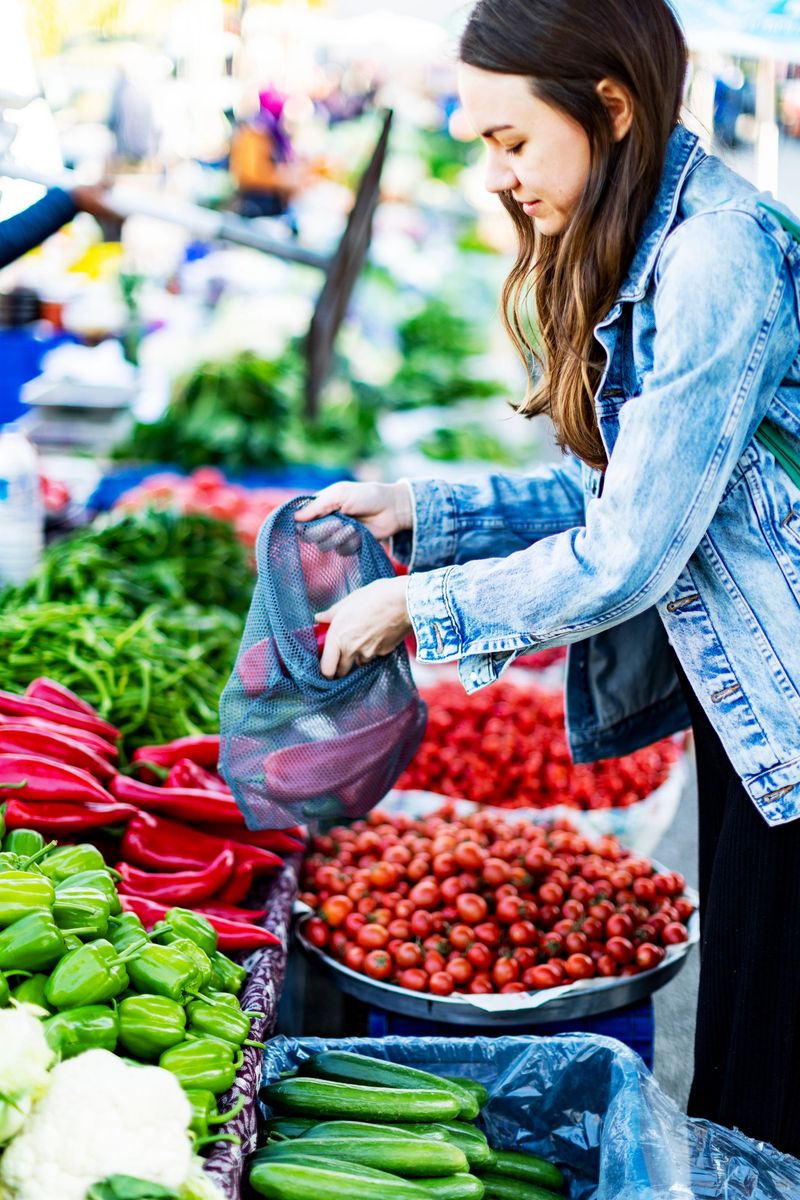 Young adult woman buying red bell pepper at market with reusable bag
