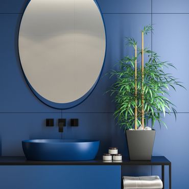 Modern blue bathroom with round mirror, sink, and potted plant.