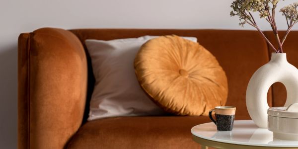 Cozy brown sofa with decorative pillows and a small coffee table with a cup and vase.