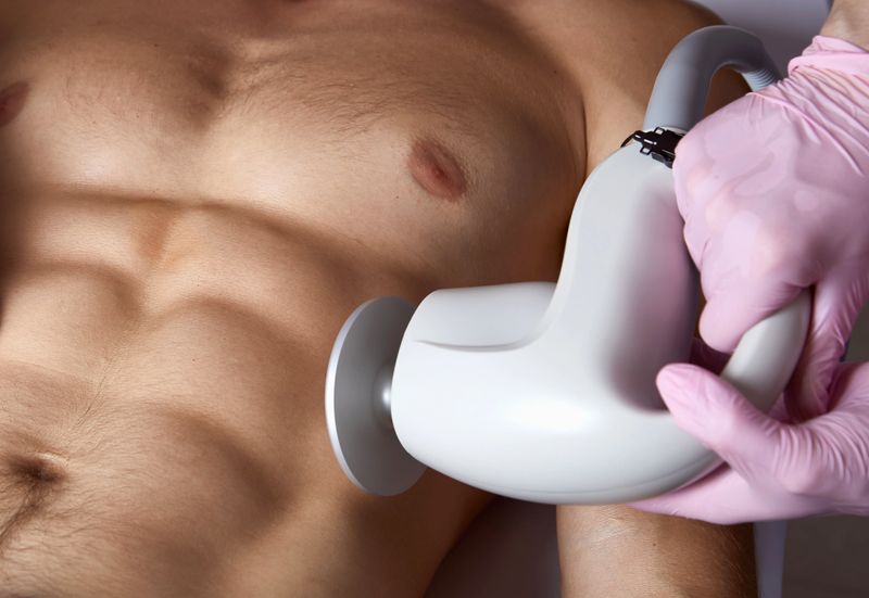 Man receiving fat reductive skin lifting body treatment on modern equipment at cosmetology clinic, male body care concept