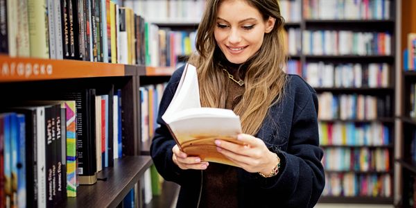 A woman reading a book in a bookstore, smiling.