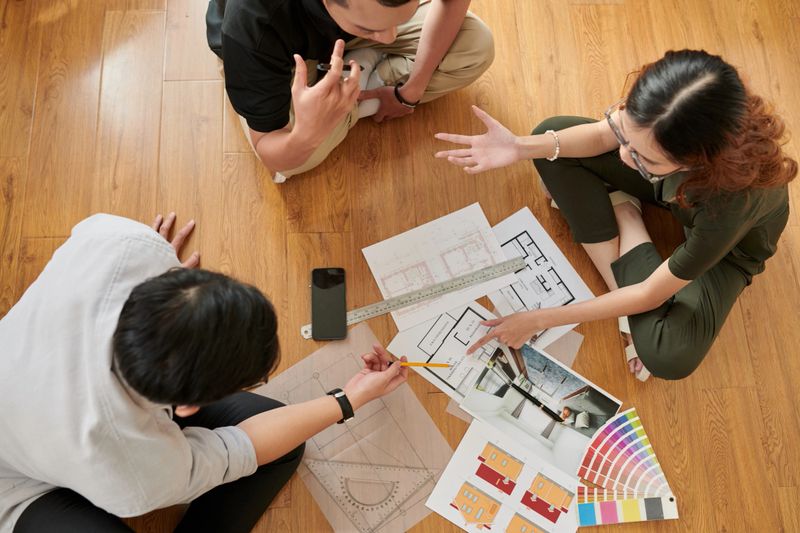 Team of young interior designers discussing new project when sitting on floor in architecture bureau, view from above