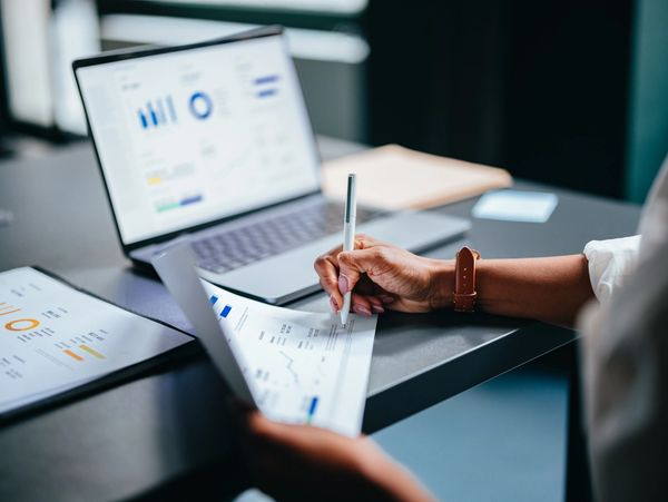 Person analyzing financial charts and writing notes beside a laptop.