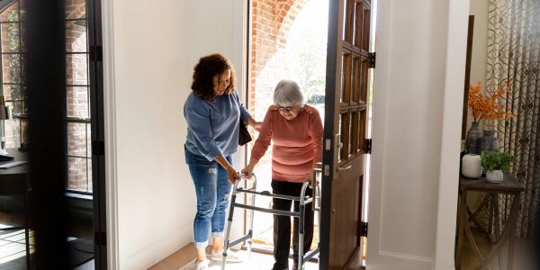 A young woman helping an elderly woman with a walker.