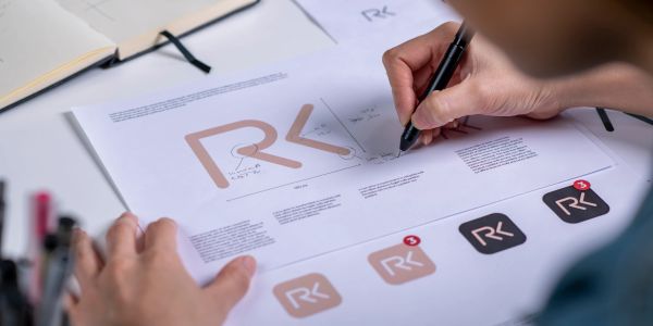 Person sketching a logo design on paper with a pen.