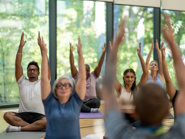 Group yoga class stretching with raised arms indoors.