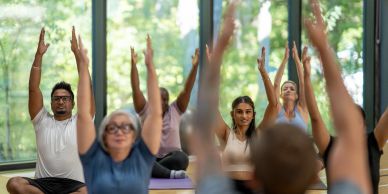 A diverse group practicing yoga indoors with arms raised.