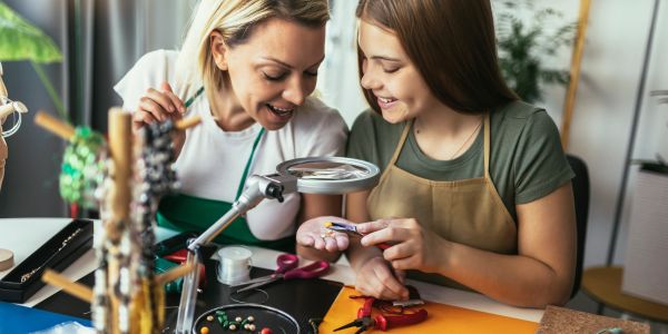 Two women crafting jewelry together happily.