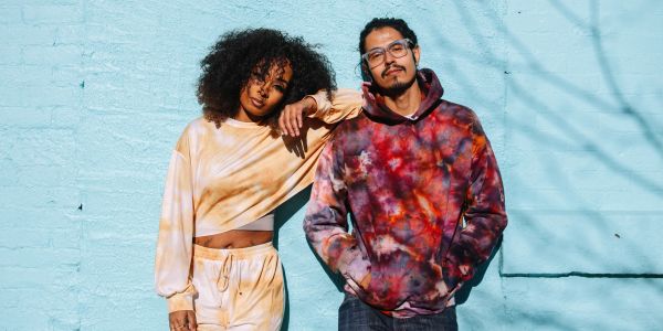 Two people in tie-dye clothing leaning against a blue wall.