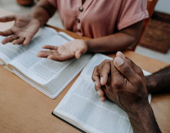 Two people discussing and praying over open books at a table.