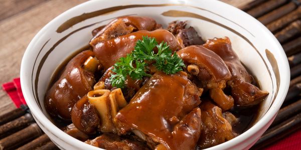 A bowl of braised pork trotters garnished with parsley.