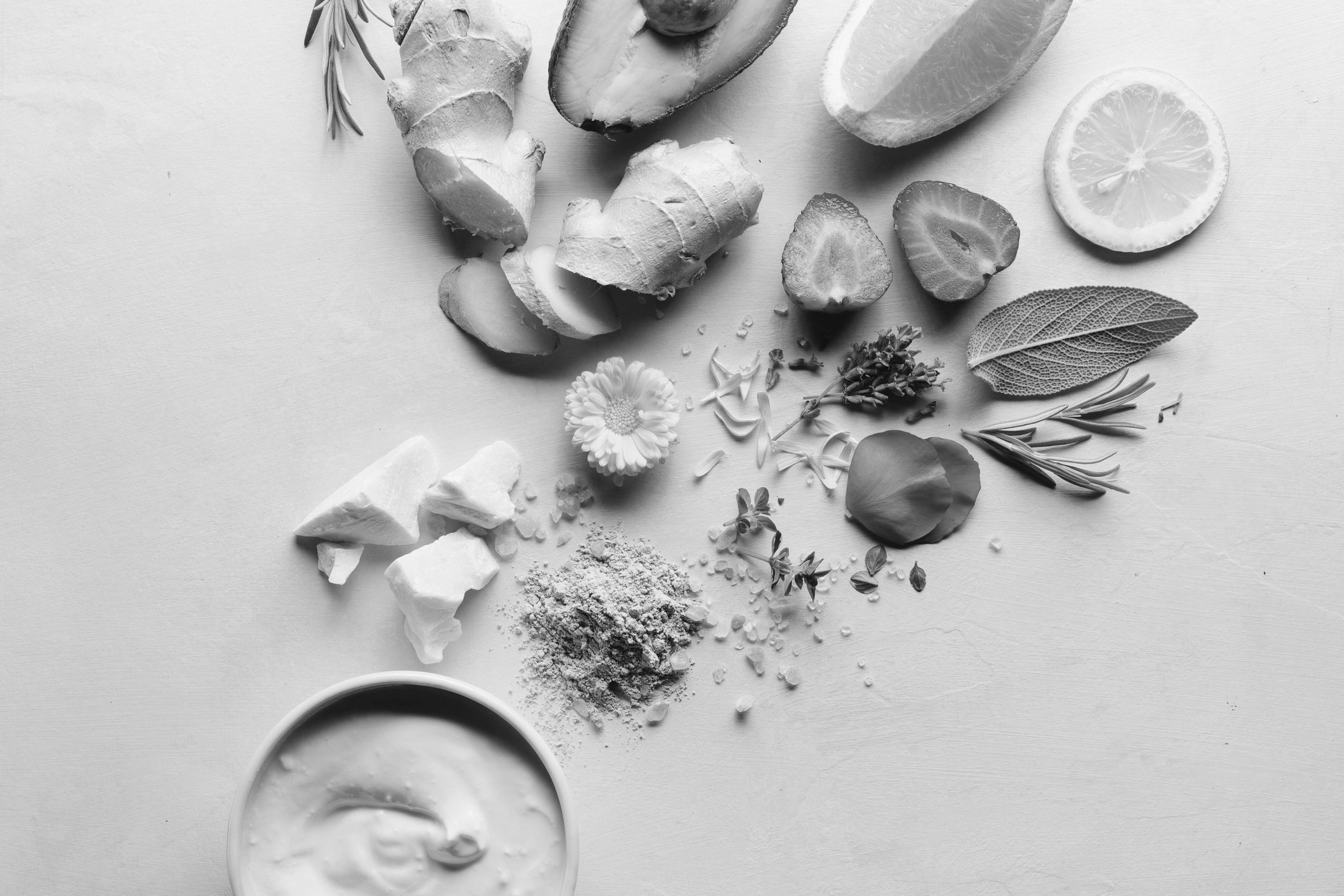 Fresh natural ingredients including ginger, avocado, citrus, and flowers on a light surface.
