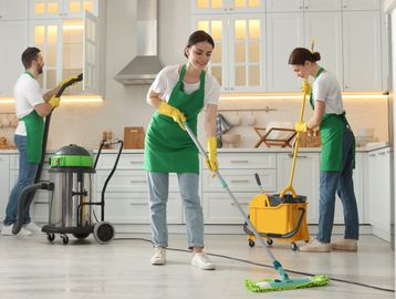 Three people cleaning a modern kitchen with mops and vacuum.