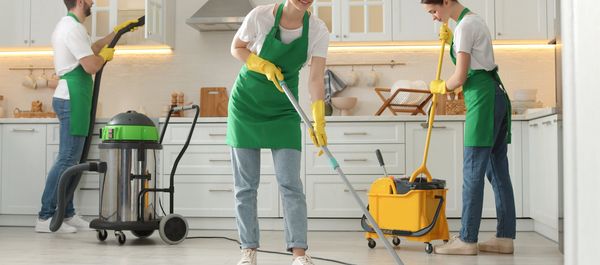 Three people cleaning a kitchen with various cleaning tools.
