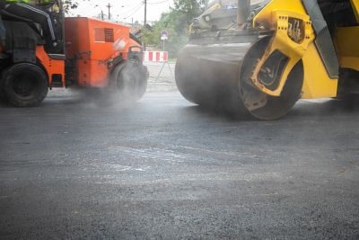 Road construction with steamroller and paving machine.