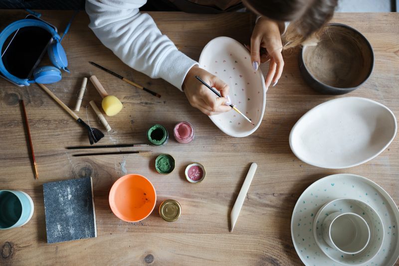 Cropped portrait of an attractive mature woman sitting alone and painting a pottery bowl in her workshop. Craftsperson painting a bowl made of clay in art studio