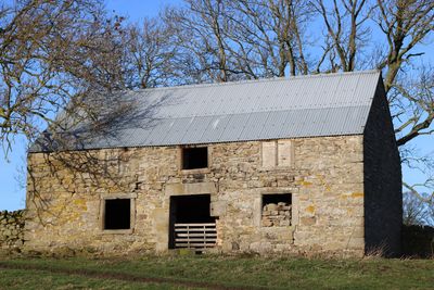 Old stone barn with metal roof under clear blue sky.