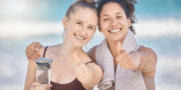 Two happy women at the beach giving thumbs up.