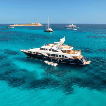Luxury yachts anchored in clear turquoise waters near a small island.