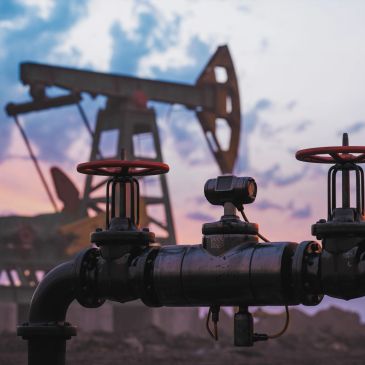 Oil pumpjack silhouette at sunset with pipeline valve close-up.