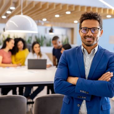 Confident businessman in blue suit stands with arms crossed in modern office.