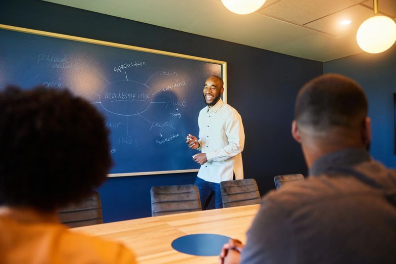 Businessman laughing while giving a marketing strategies presentation to coworkers sitting at a board room table in an office