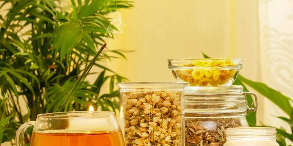 Glass jars of dried herbs and a cup of tea on a wooden table.
