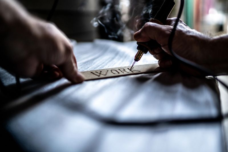 Close-up of a man writing on wood with pyrograph at home