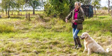 Woman whistles while training a golden retriever outdoors in a grassy field.