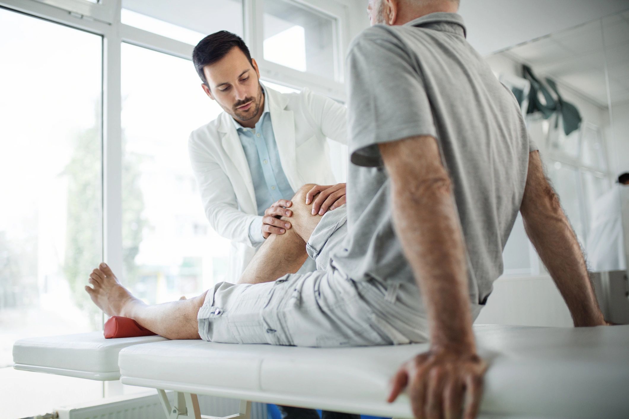Doctor examining elderly man's knee in clinic.