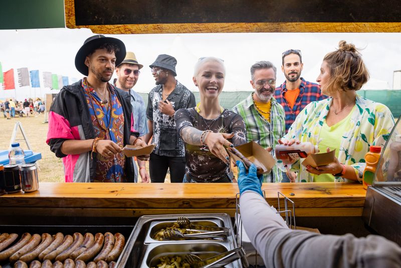 Group of mixed age and ethic friends ordering at a food stall at a festival in Northumberland, North East England. An unrecognisable person is handing a woman her food.
