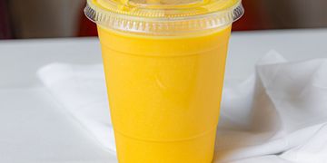 A plastic cup filled with bright yellow mango smoothie.