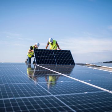 Two workers installing solar panels on a rooftop.