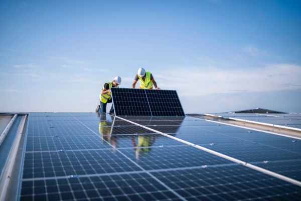 Two workers installing solar panels on a roof.