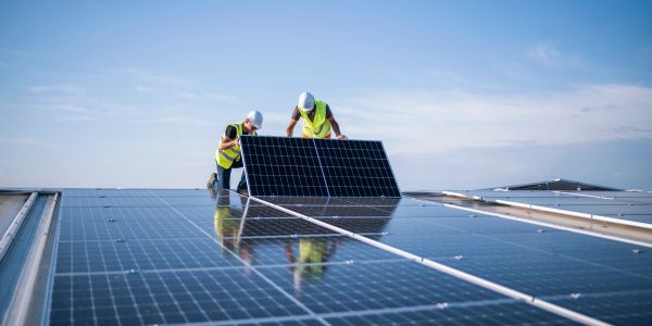 Two workers installing solar panels under clear blue sky.