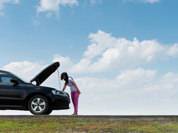 A woman checking the engine of a black car on a clear day.