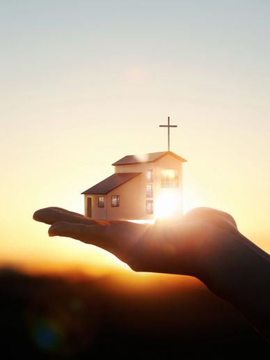 Hand holding a small church model with sunlight shining through.