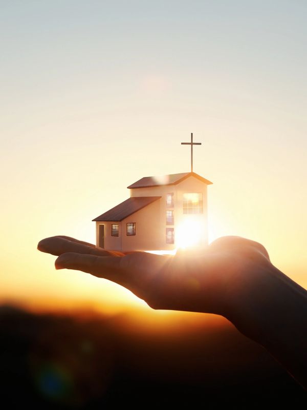 Hand holding a small church model with sunlight shining through.