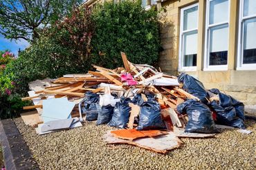 Pile of construction debris and black garbage bags outside a house.