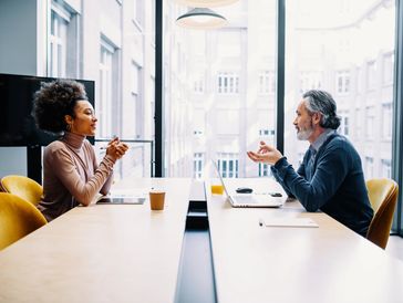 Deux personnes échangent sérieusement autour d’une table, dans un bureau moderne et lumineux.