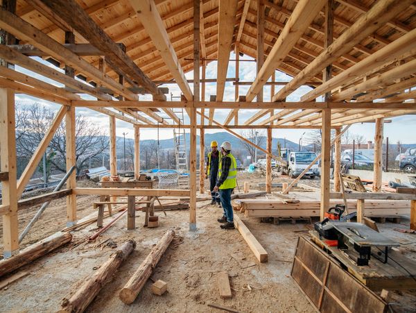 Two construction workers discussing inside a wooden framework of a building under construction.