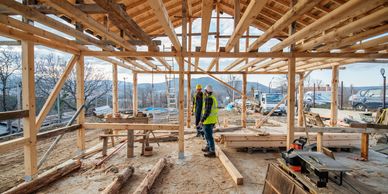 Two construction workers discussing inside a wooden framework of a building under construction.