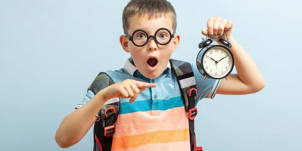 Surprised boy with glasses holding a clock.