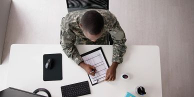 Military personnel writing on a clipboard at a desk.