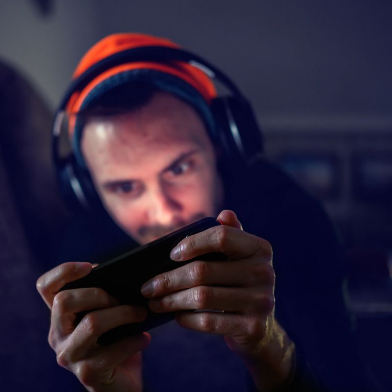 A young gamer plays mobile games on the sofa in the evening at home