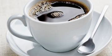 A white cup filled with black coffee on a matching saucer with a spoon.