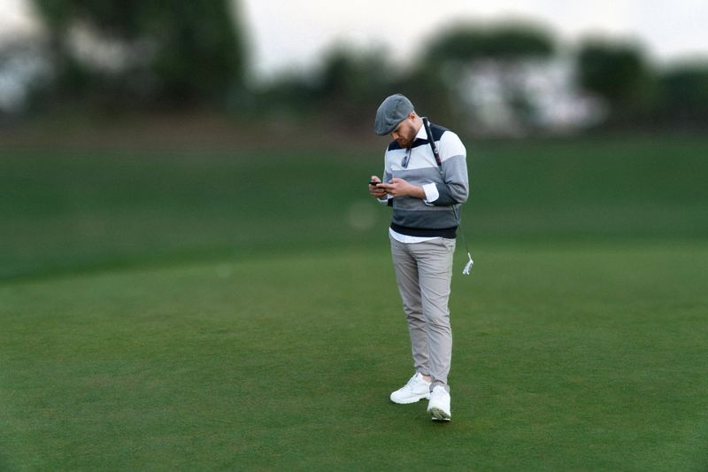 Portrait of a golf player using the phone on the golf course. Horizontal shot.